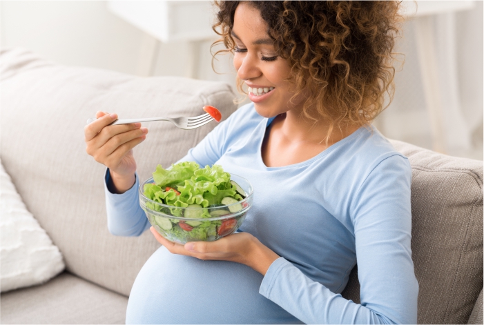 Mulher morena grávida comendo um prato de verduras