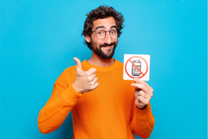 Homem de blusa laranja segurando cartaz que mostra o símbolo de proibido celular. 