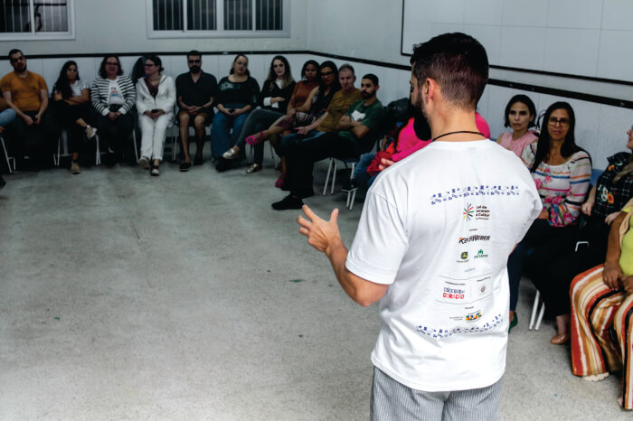 Homem de costas falando para pessoas sentadas 