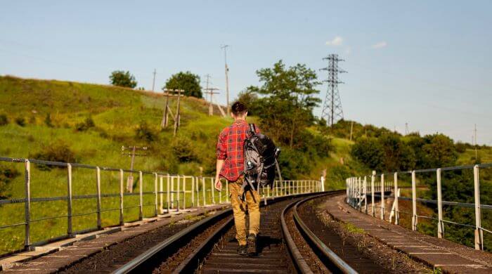 Homem de mochila caminhando sobre trilhos