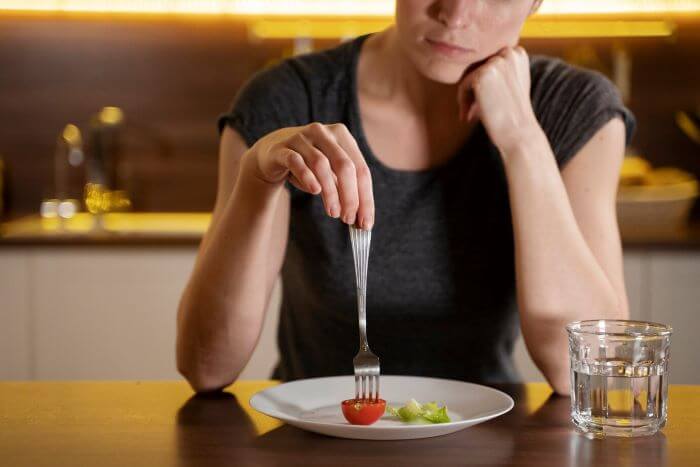 Mulher comendo pedaço de tomate com garfo