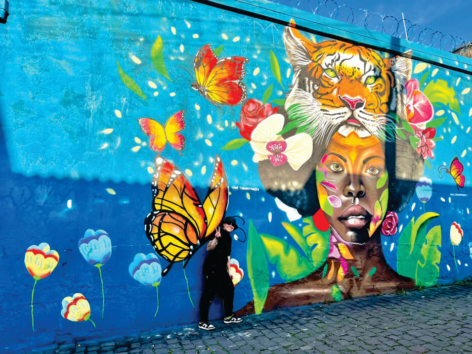 Pessoa em frente a muro com mulher, borboletas e flores pintadas