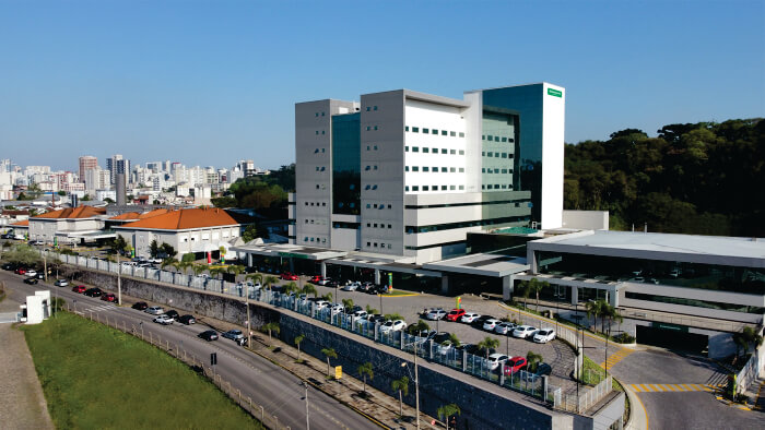 Foto aérea de grande prédio com estacionamento e outros prédios ao fundo