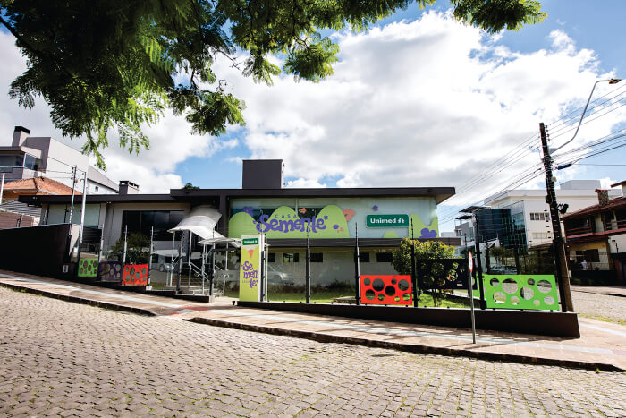 Casa verde com decorações coloridas e logo da Unimed